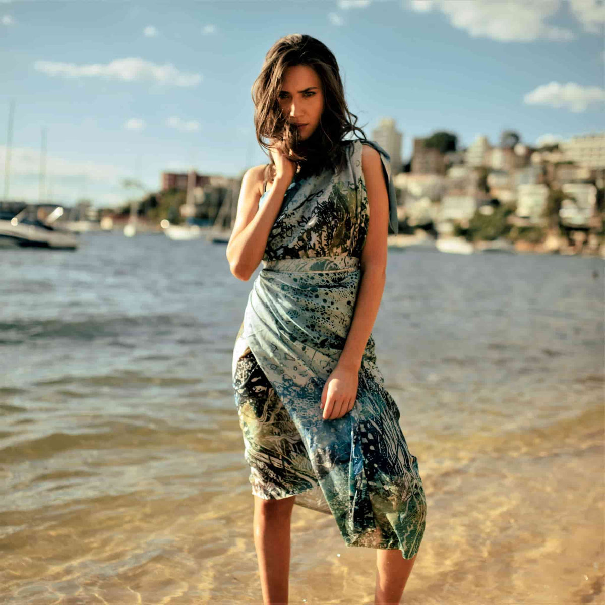 The Swim silk cotton sarong styled into a short wrap dress at the beach. Showing the vibrant blues and greens of a summer holiday by the water.